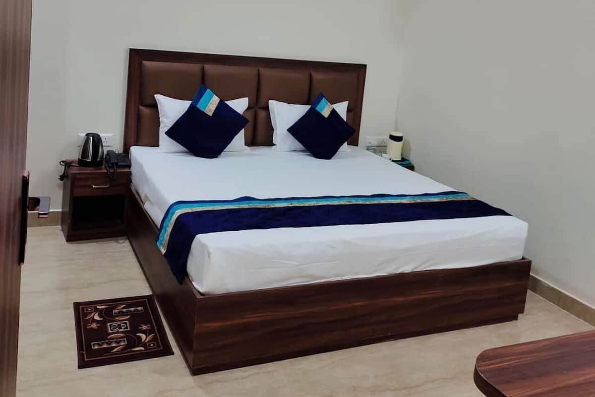 Quarto de hotel com uma cama grande, mesa de cabeceira com telefone e chaleira, uma mesinha e ar condicionado fixado na parede.