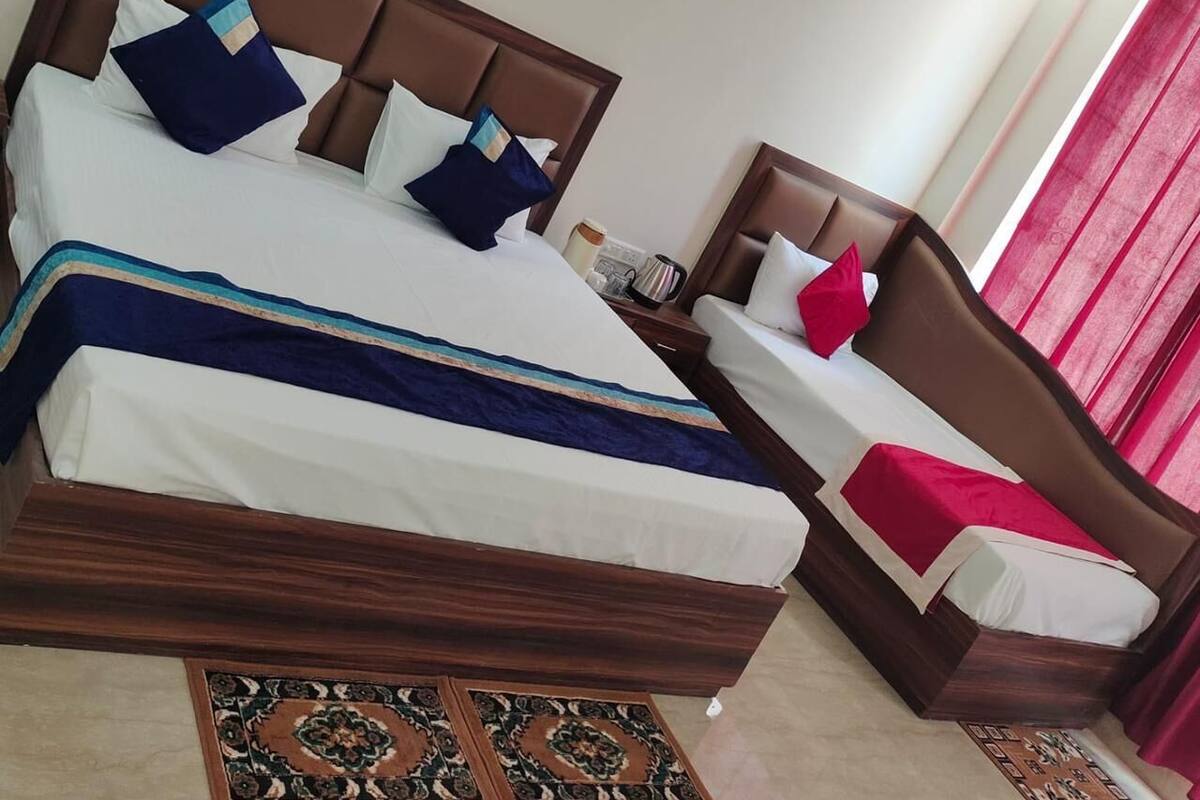 Uma cama de casal com cabeceira de madeira, uma mesinha de cabeceira com abajur e uma cortina vermelha.