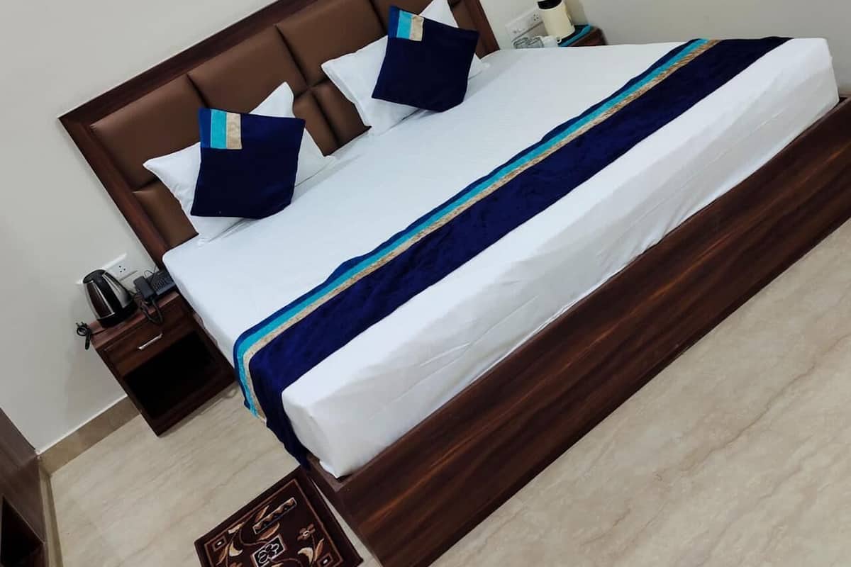 Cama bem arrumada com cabeceira de madeira, roupa de cama branca e colcha listrada em azul e branco. Há uma mesa de cabeceira com abajur, telefone e um pequeno objeto decorativo.