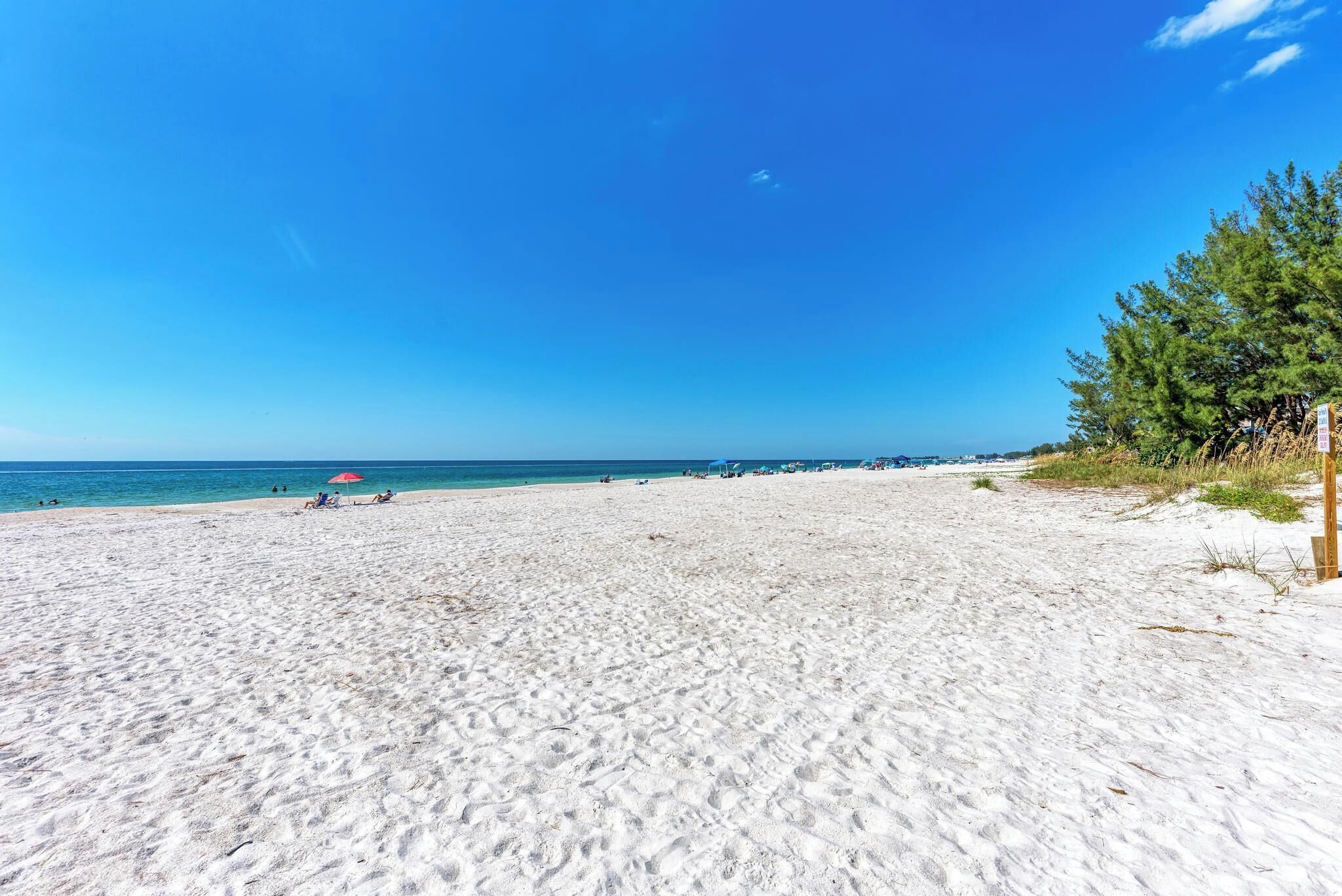 A beach with white sand, clear blue sky, and a calm sea.