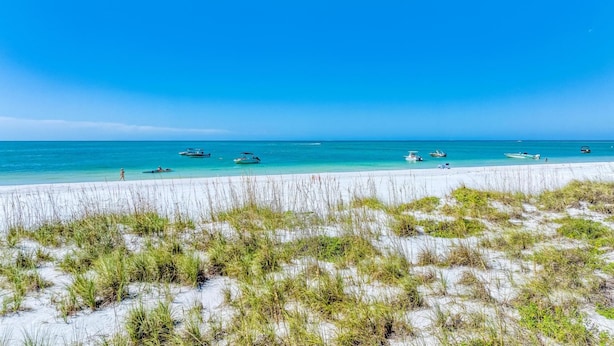 Ein Strand mit weißem Sand, klarem, blauem Wasser und mehreren Booten.