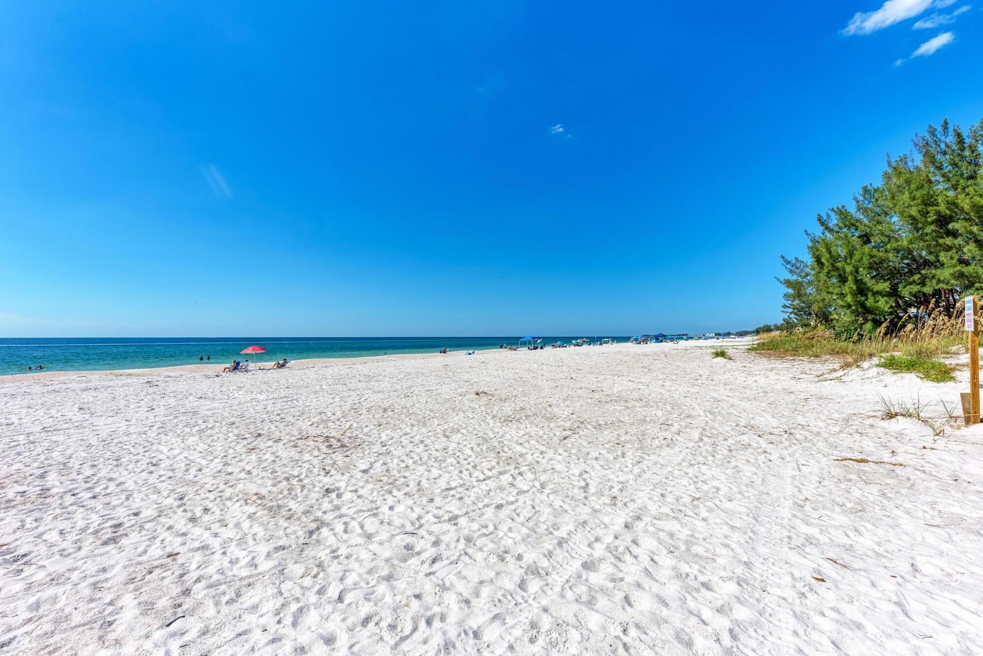 Ein Strand mit weißem Sand, blauem Himmel und einigen wenigen Personen.
