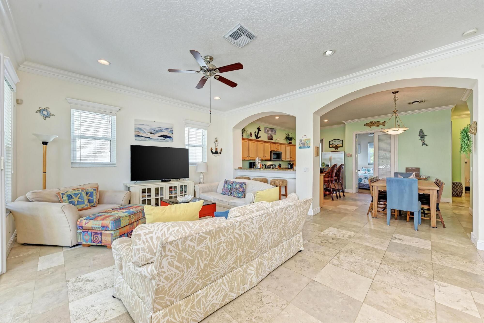 A spacious living room with a large TV, a ceiling fan, and a kitchen area with wooden cabinets and a dining table.