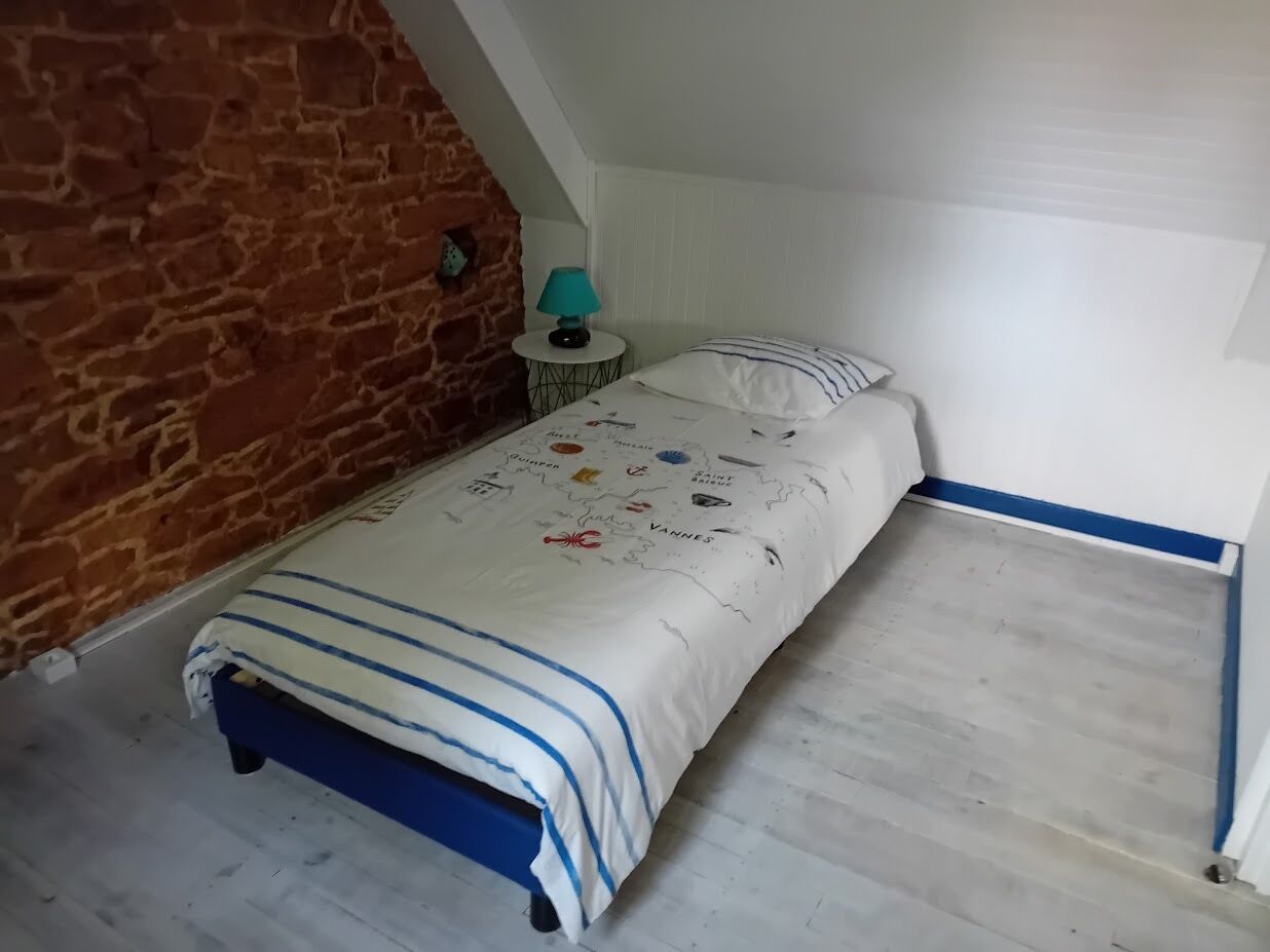 A bedroom with a bed, a lamp, and a brick wall.
