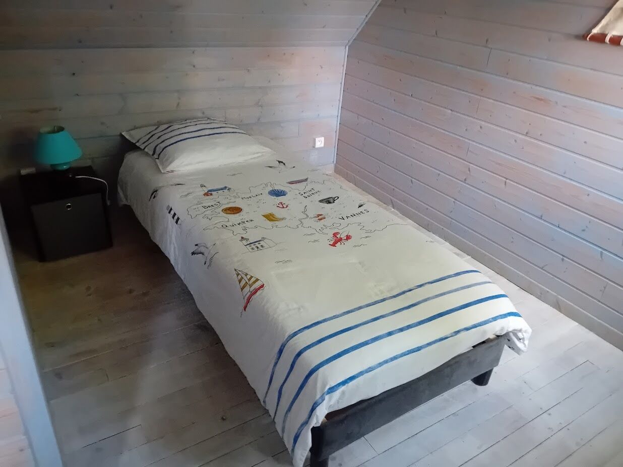 A small, single-bed room with a wooden floor and sloped ceiling, featuring a bed with a white and blue striped bedspread and a map-themed pillow.