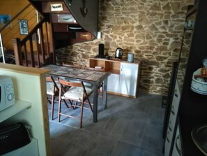 Une cuisine avec un mur en pierre, une table à manger en bois avec des chaises et un meuble blanc.
