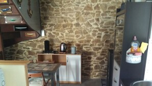 Une cuisine de taille réduite avec des murs en pierre, une petite table à manger et des appareils électroménagers de base.