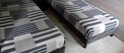 A room with two beds, each with a striped bedspread, a small table with a lamp, and wooden flooring.