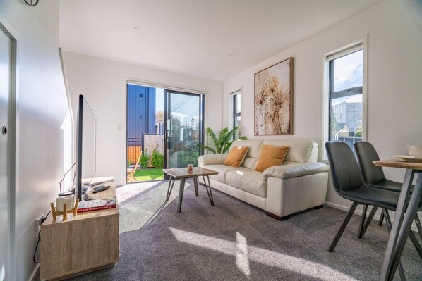 A modern living room with a sofa, coffee table, and chairs, a balcony with a view, and a painting on the wall.