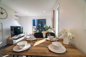 Un coin repas avec une table en bois dressée pour quatre personnes, un téléviseur et une vue sur l’extérieur.