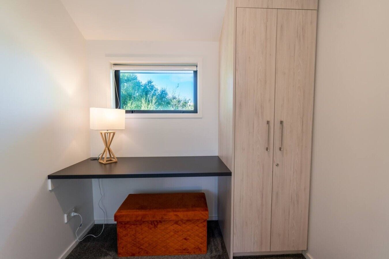 A room with a desk, a lamp, a window, a wardrobe, and a storage box.