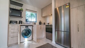 Una cucina moderna con lavatrice integrata, forno, frigorifero, mobili in legno e una finestra vista alberi.