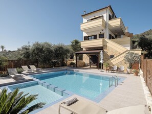 A modern two-story building with a swimming pool, outdoor seating, and a stone facade.