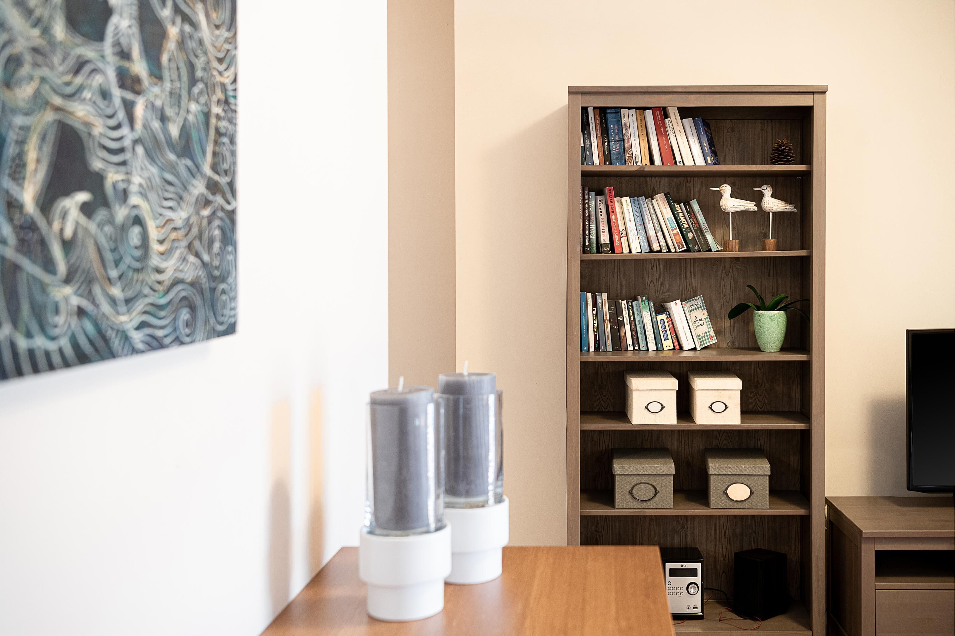 Una sala de estar moderna con una estantería de madera, un cuadro y una mesa con velas decorativas.