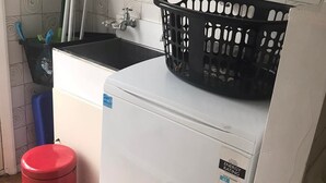 Une petite cuisine équipée d’un lave-linge, d’une poubelle rouge et d’un panier à linge noir posé sur le dessus de la machine.