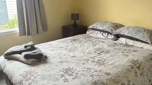 Une chambre à coucher avec une couvre-lit à motifs floraux, deux oreillers, une lampe de chevet et une fenêtre avec des rideaux.