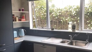 Une cuisine compacte dotée d’un lave-vaisselle encastré, d’un évier à deux bacs et d’une fenêtre donnant sur un jardin.