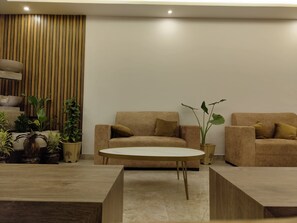 A modern living room with a sofa, armchairs, a coffee table, and potted plants.