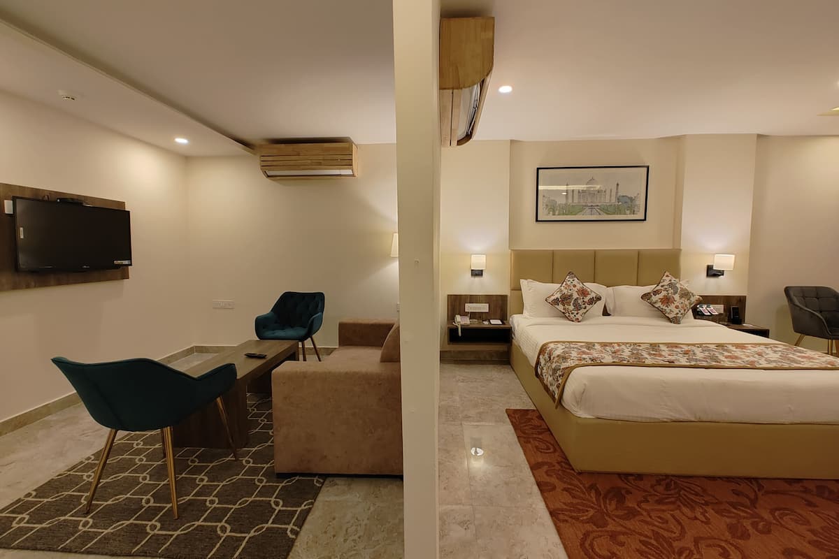A hotel room with a bed, a desk, a chair, a television, and a wall-mounted air conditioner.