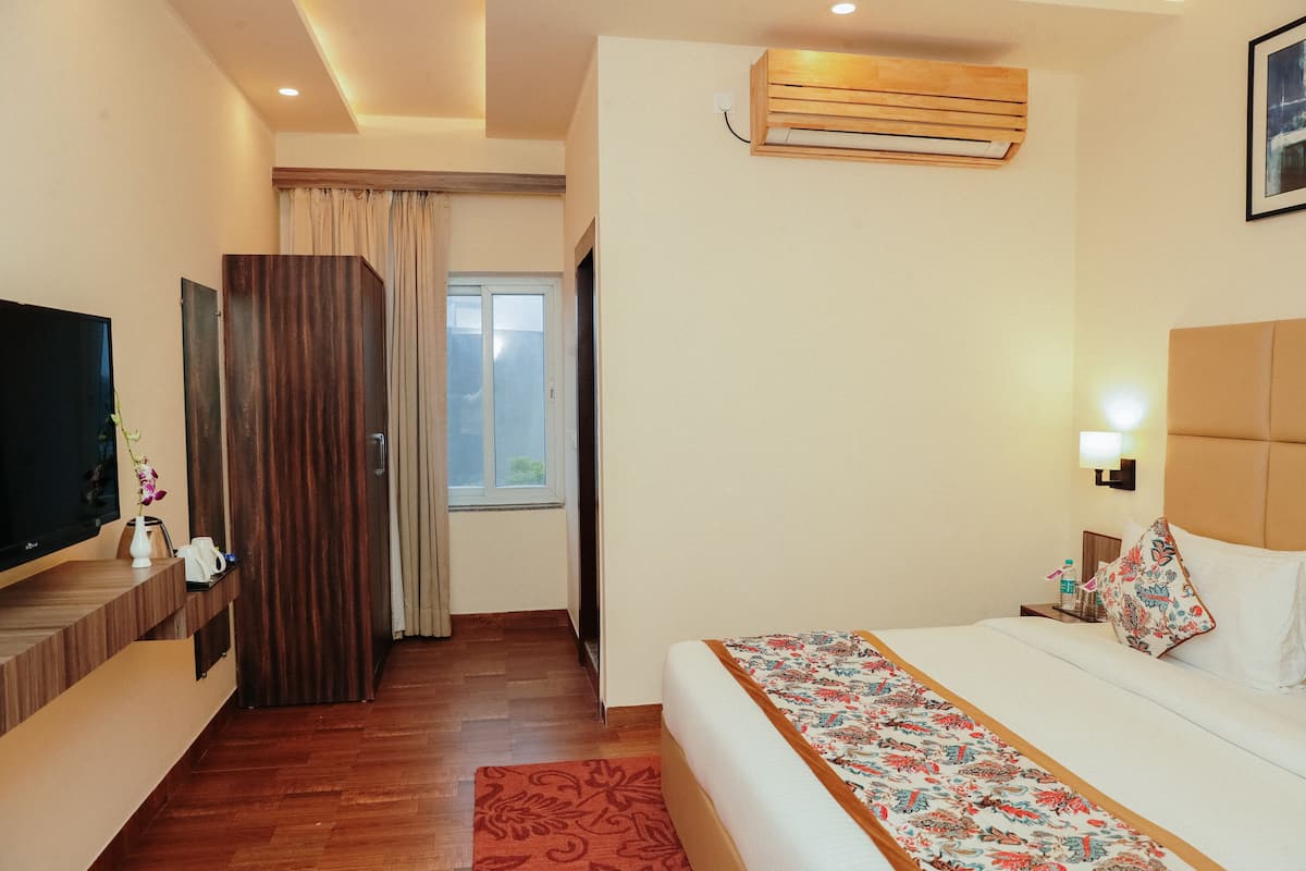 A hotel room with a bed, a TV, a wardrobe, a window, and an air conditioning unit.