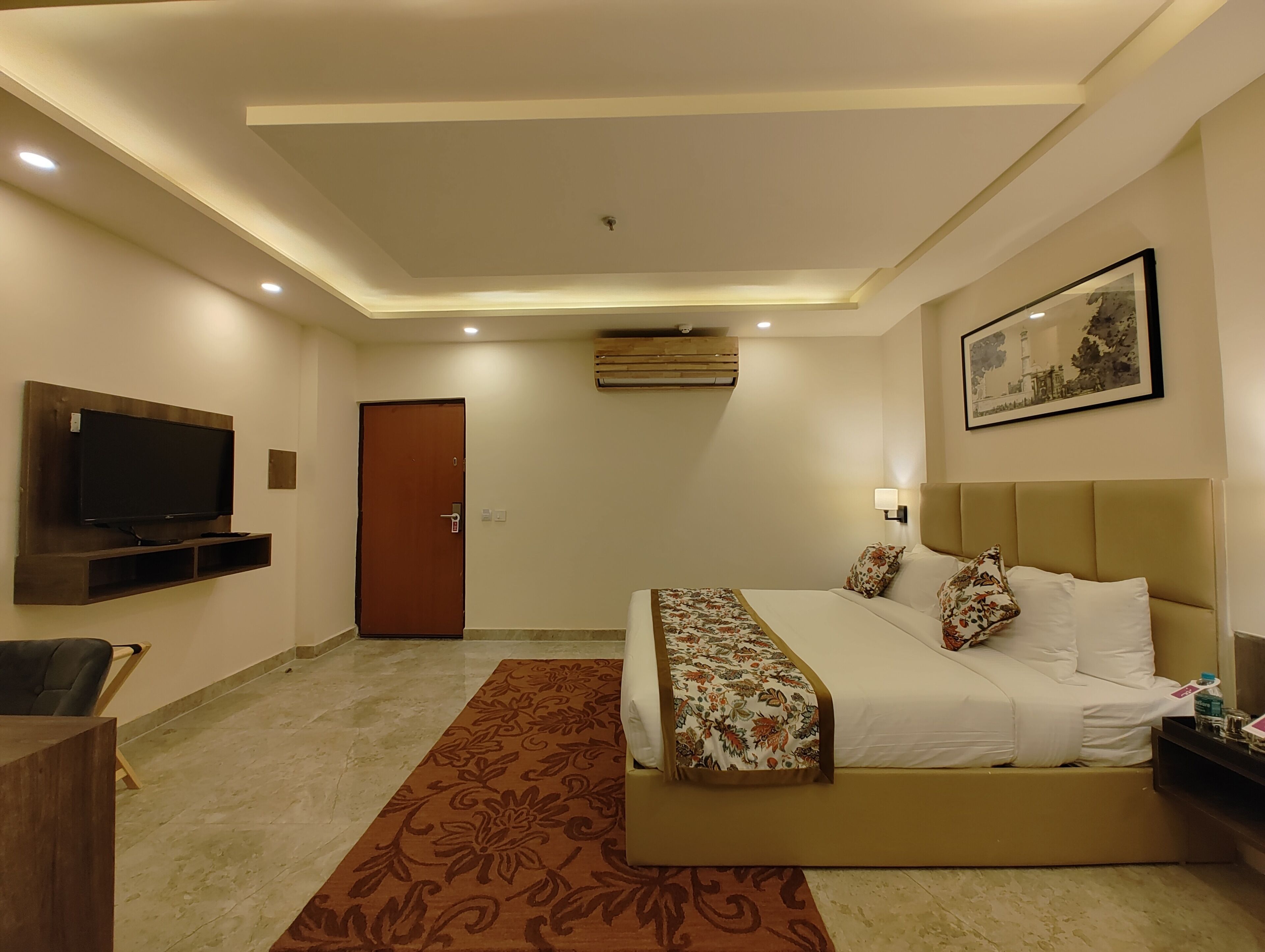 A hotel room with a bed, a television mounted on the wall, a door, and a framed picture on the wall.