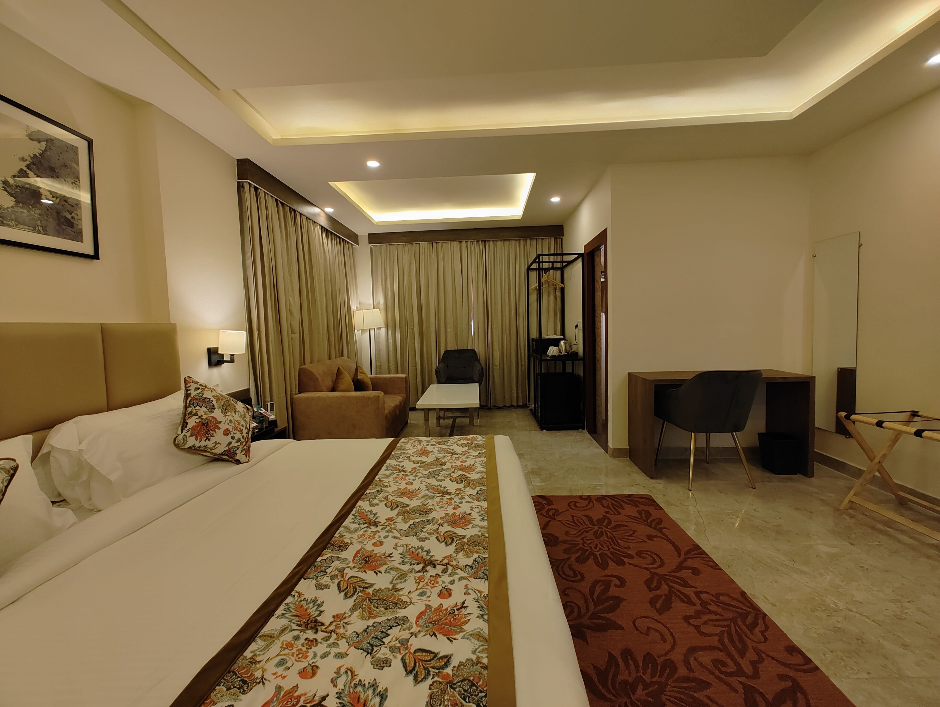 A hotel room with a bed, a sofa, a desk, a chair, a mirror, and curtains.