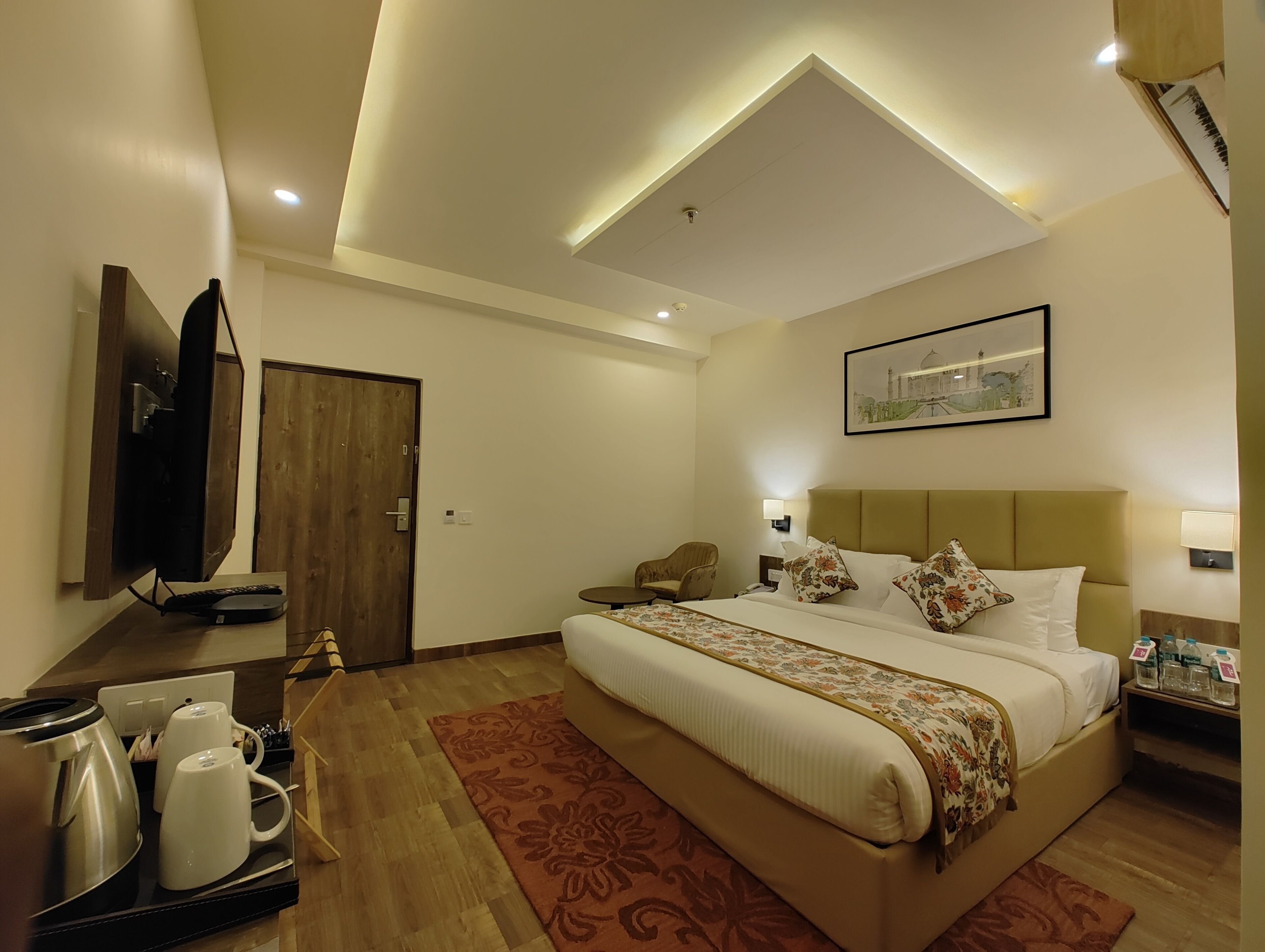 A hotel room with a bed, bedside table, lamp, and a television mounted on the wall.