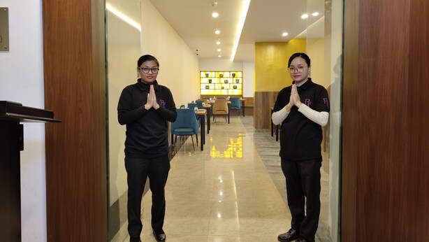 A hotel corridor with a wooden door frame, a glass wall, and a seating area in the background. - Regenta Inn Greater Noida (Greater Noida)