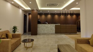 A modern reception area with a marble reception desk, wooden paneling, and a seating area with sofas and a coffee table. - Regenta Inn Greater Noida (Greater Noida)