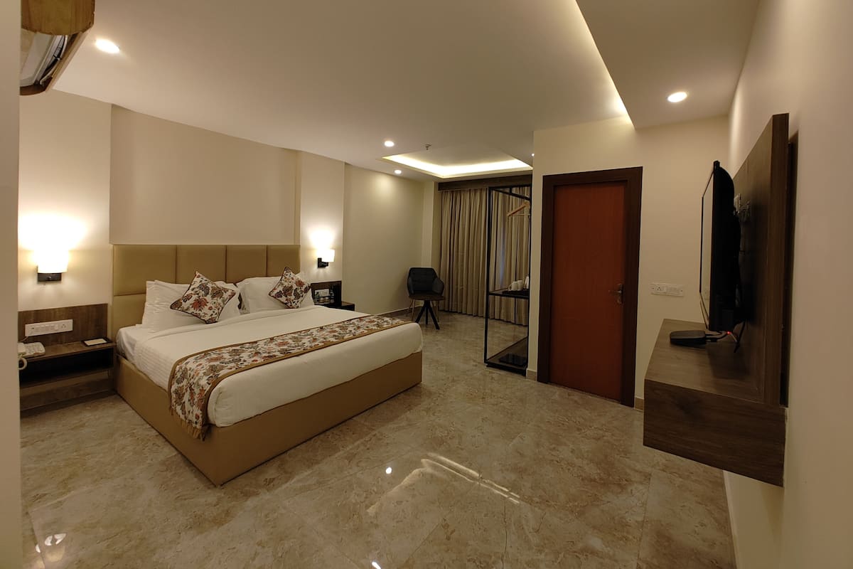 A hotel room with a large bed, bedside tables, a TV, a mirror, and a door.