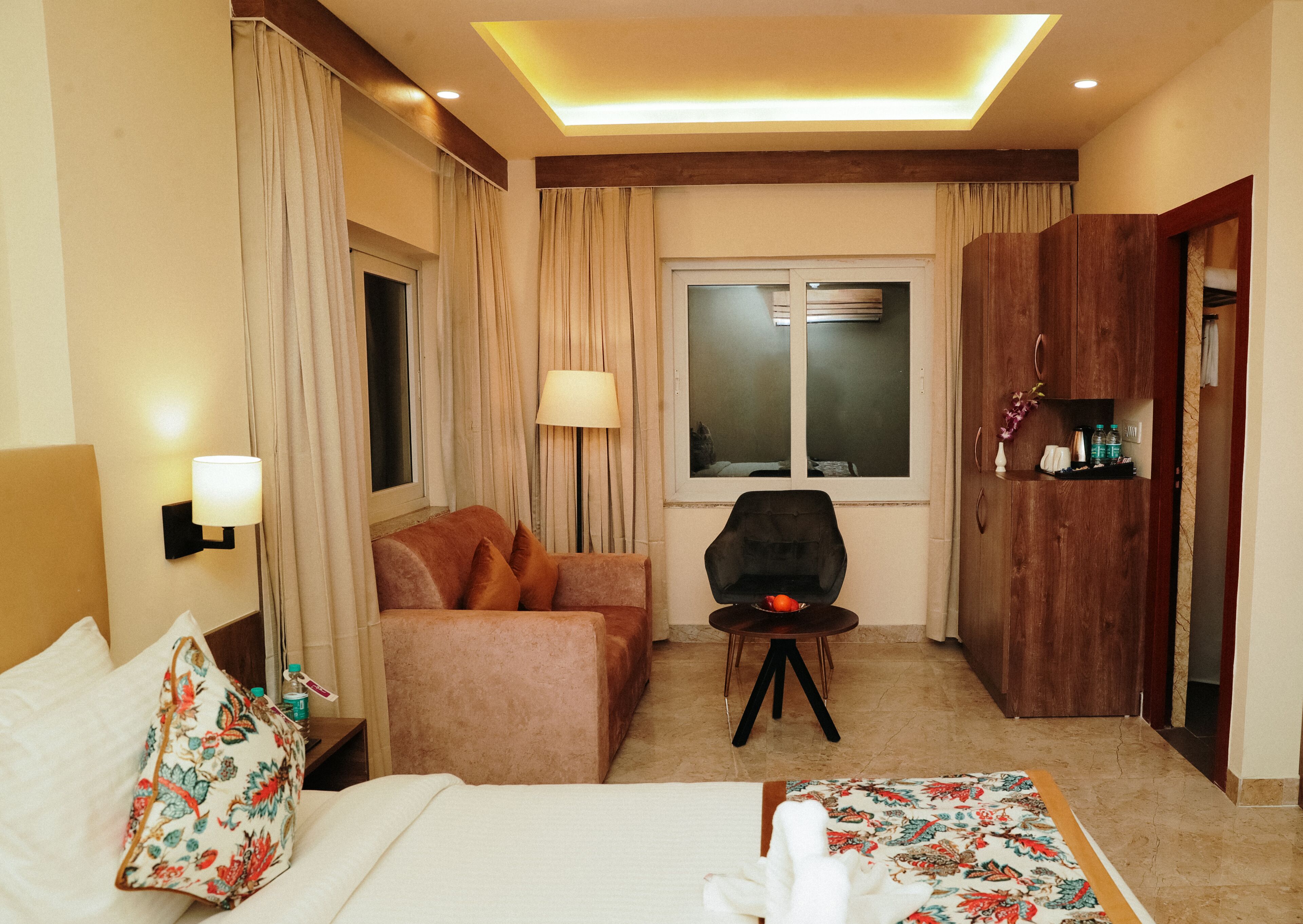 Ein Hotelzimmer mit einem Bett, einem Sofa, einem kleinen Tisch mit einer Obstschale, einer Lampe und einem Kleiderschrank.