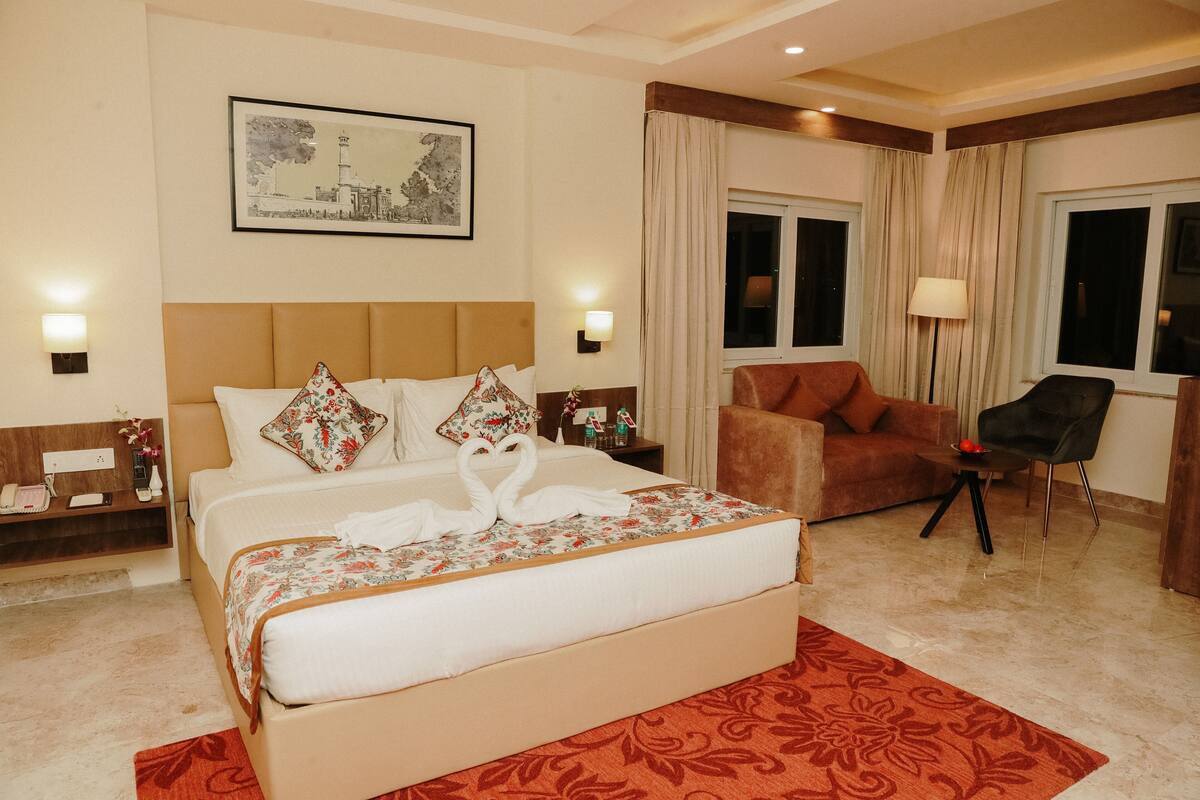 A hotel room with a large bed, a sofa, a chair, a desk, and a window with curtains.