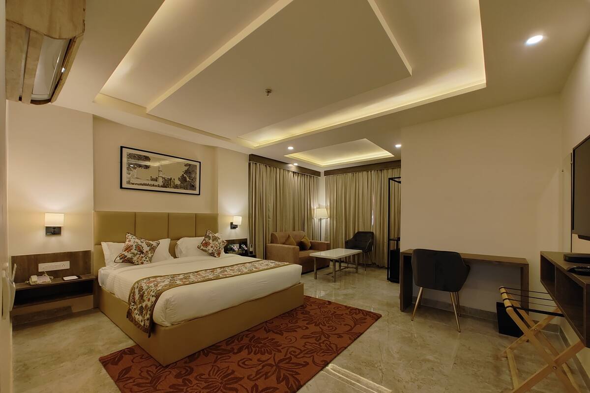A hotel room with a large bed, a desk, a chair, a television, and a painting on the wall.