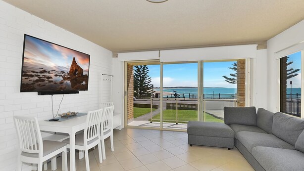 Una sala de estar moderna con un televisor grande, un comedor y un balcón con vista al mar.