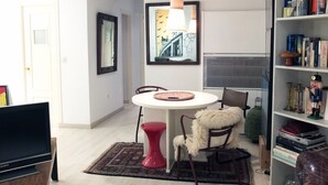 Ein Wohnzimmer mit rundem Tisch, einem roten Hocker, einem Bücherregal und einem Fernseher.