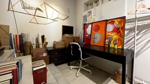 Ein Zimmer mit Schreibtisch, Stuhl, Regalen mit Aufbewahrungsboxen und einer Pendelleuchte.