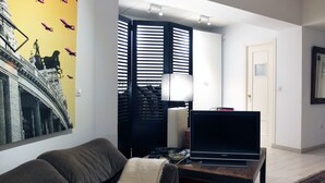 Ein Wohnzimmer mit einer Couch, einem Flachbildfernseher, einer Lampe und einer Wand mit einem Wandgemälde mit Muster.