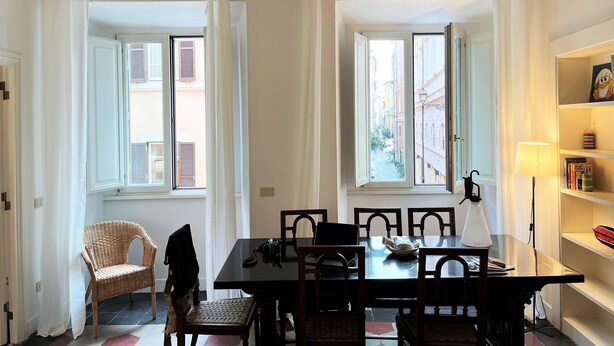 A dining area with a table, chairs, and a wicker chair. - APARTMENT 6 CASTEL SANT'ANGELO RELAIS (Roma)