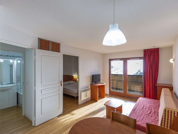 A compact hotel room with a bed, a TV, a small table, and a window with curtains.