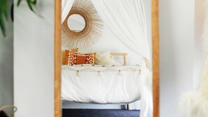 Una cama con dosel, un espejo redondo y un taburete de madera.