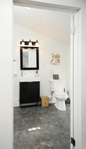 A bathroom with a white sink, black vanity, and a white toilet. There is a mirror with lights above it and a decorative sign on the wall. - Penthouse in historic brothel, drenched in sunlight! (Louisville)