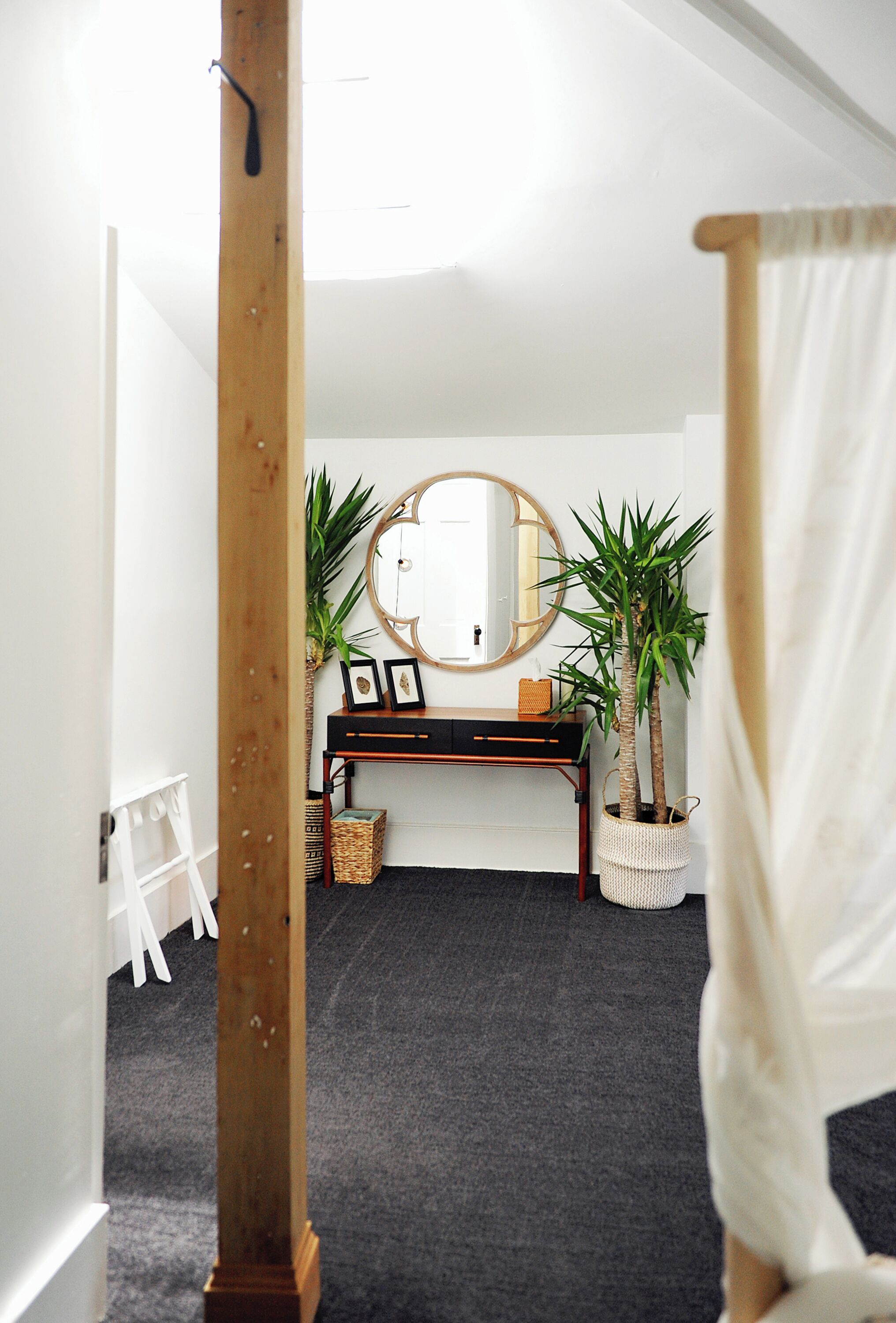 A room with a desk, a mirror, two potted plants, and a white curtain.