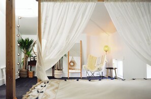 Ein Schlafzimmer mit Himmelbett, einem Sessel, einer Lampe und einem Spiegel.