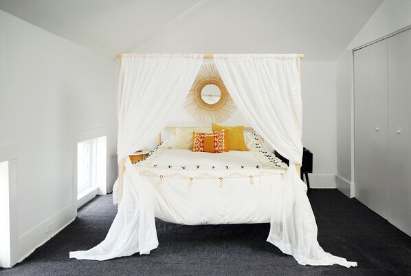 A bedroom with a four-poster bed, a round mirror above it, and a dark carpeted floor. - Penthouse in historic brothel, drenched in sunlight! (Louisville)