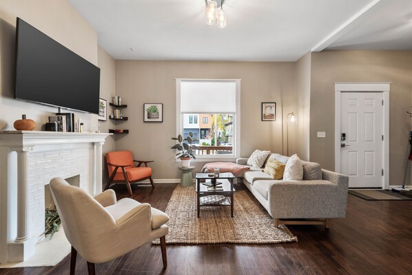 A living room with a fireplace, a television mounted on the wall, and a large window.