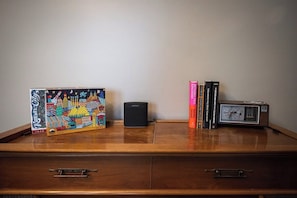 A wooden desk with a board game, a speaker, books, and a clock.