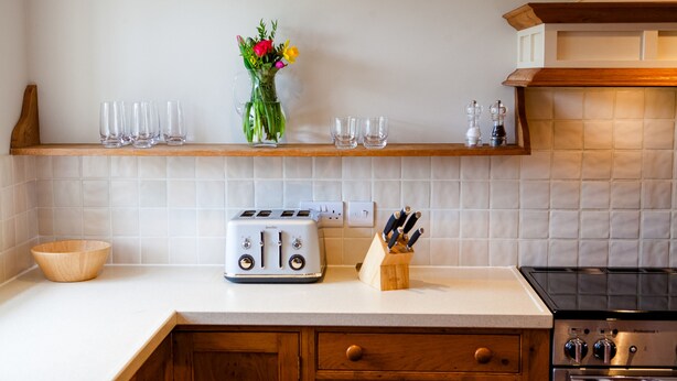 Eine Küche mit weißer Arbeitsplatte, Holzschränken, einem Toaster, einer Blumenvase und einem Herd.