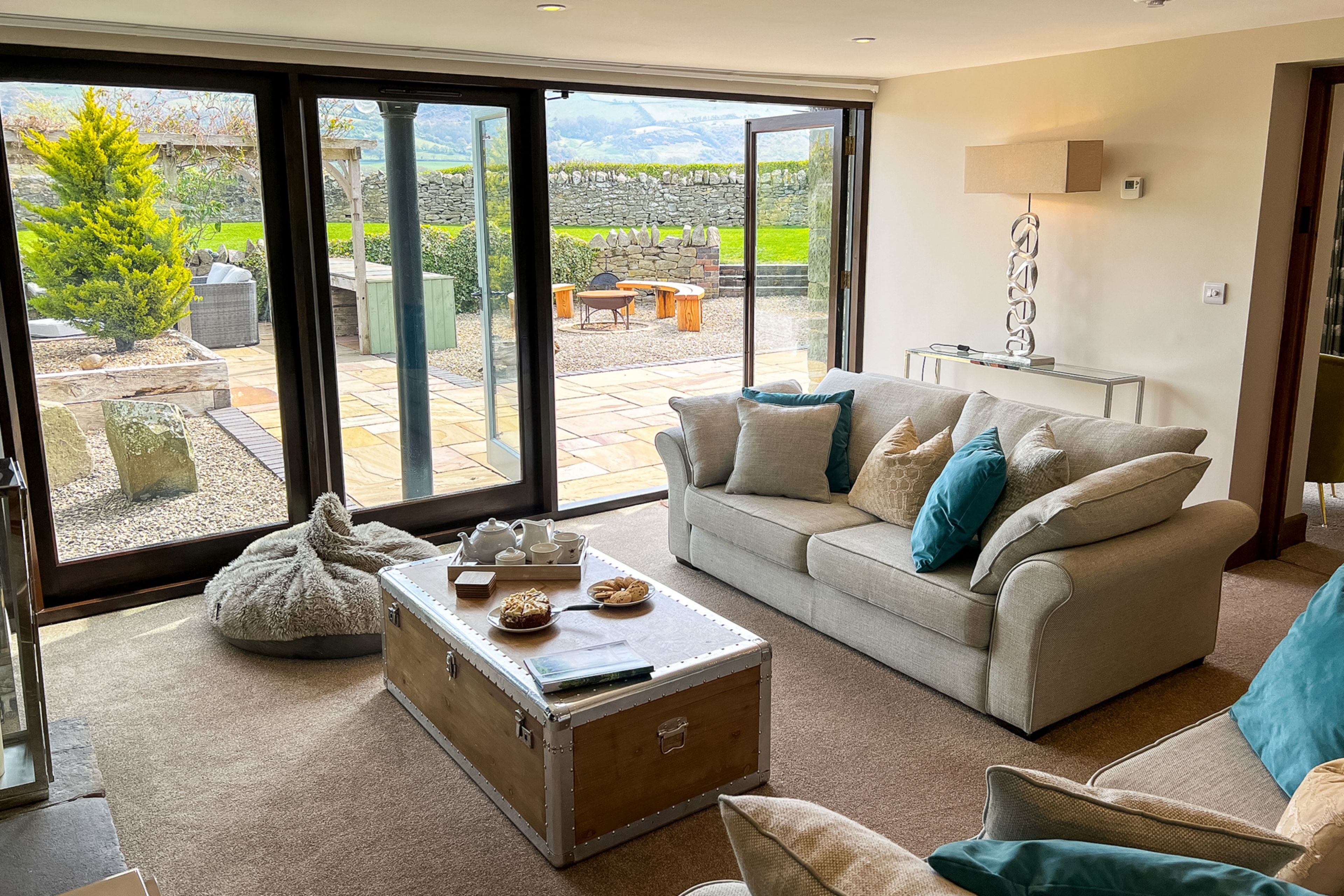 A modern living room with a sofa, a coffee table, and a view of a garden through large glass doors.