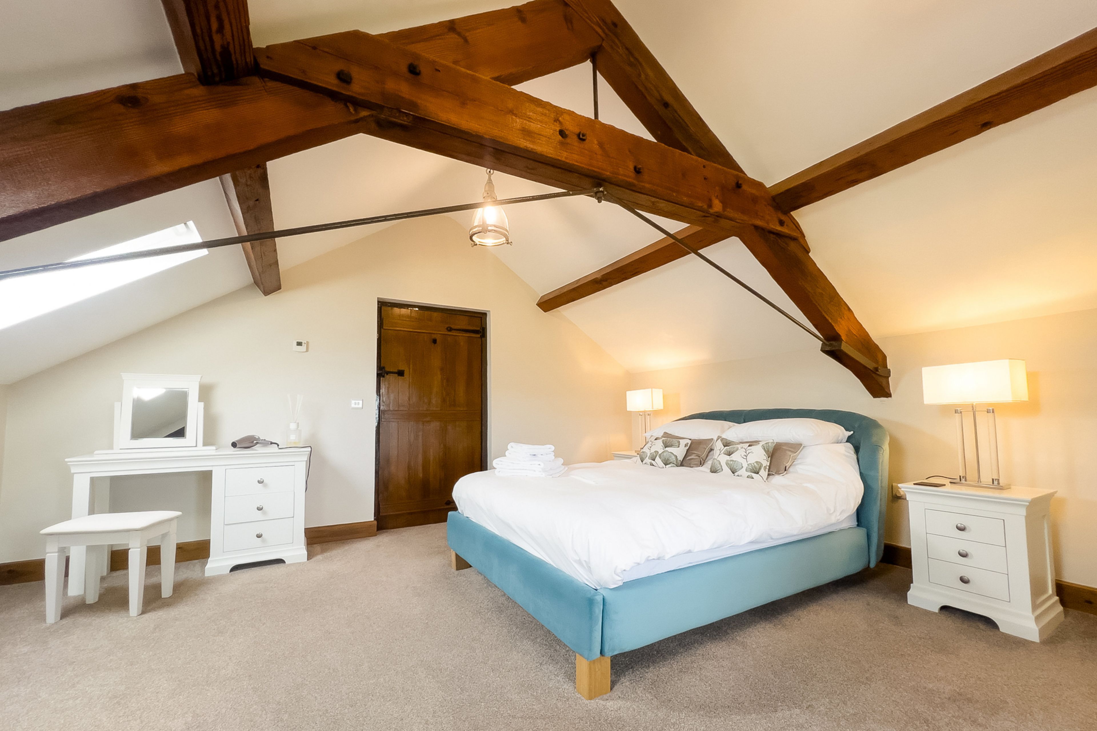 A bedroom with a sloped ceiling, a bed, bedside tables, a dresser, and a mirror.