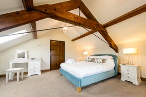 A bedroom with a sloped ceiling, a bed, bedside tables, a dresser, and a mirror.